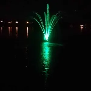 Illuminated green fountain at night reflecting in water.